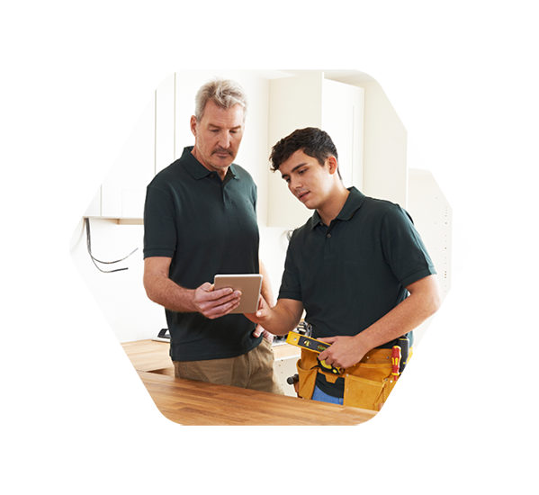 An installer and an apprentice reviewing kitchen installation details on a tablet, standing in a partially completed kitchen.