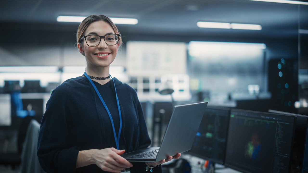 A woman wearing glasses holds a laptop.