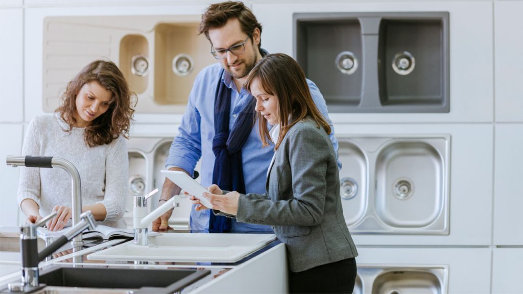 Three individuals inspecting a sink in a modern kitchen.