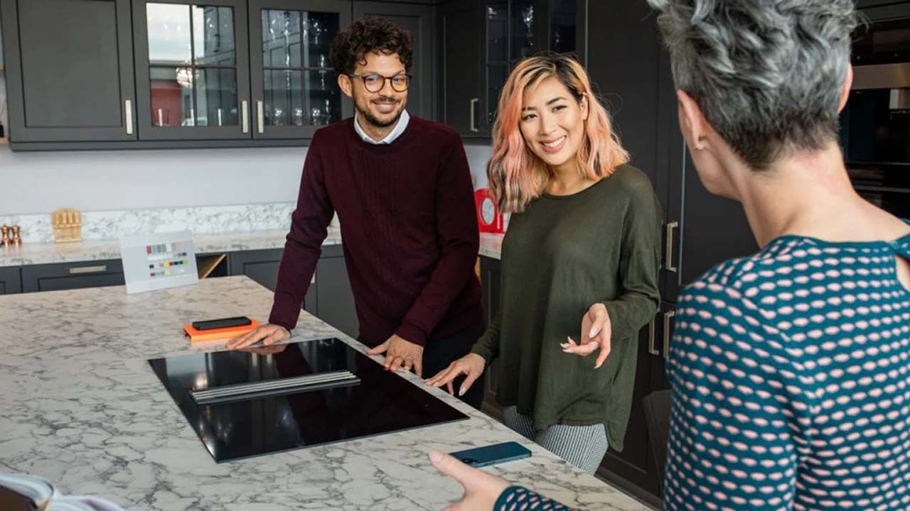 A couple and a woman stand together in a modern kitchen.