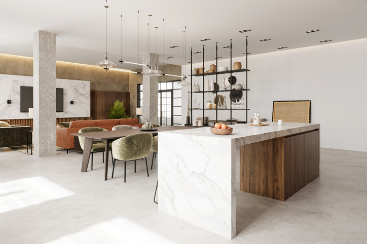 A spacious, open-plan kitchen and dining area with a large marble island. The room features a mix of modern and rustic design elements, including exposed concrete, wooden accents, and contemporary furniture.