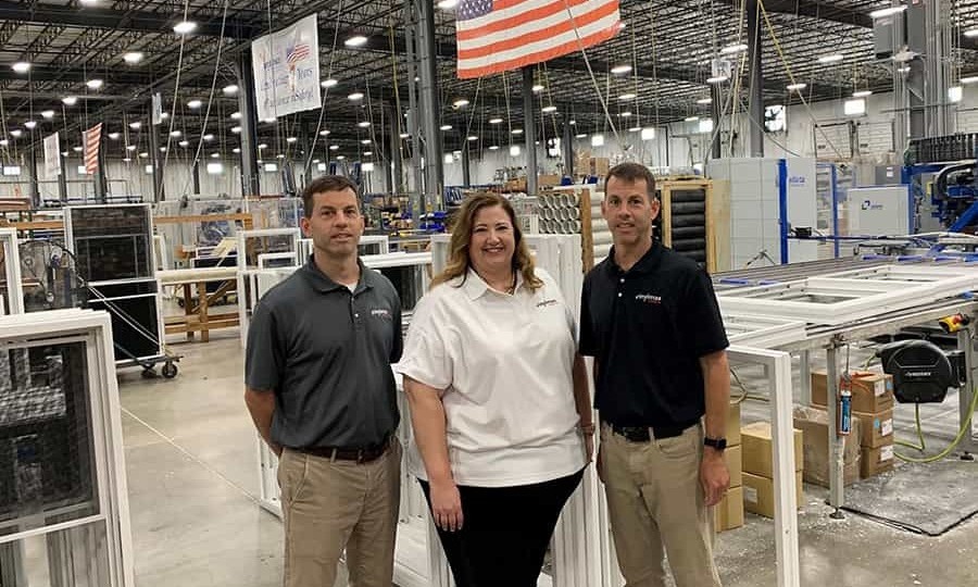 Three individuals stand before a large factory