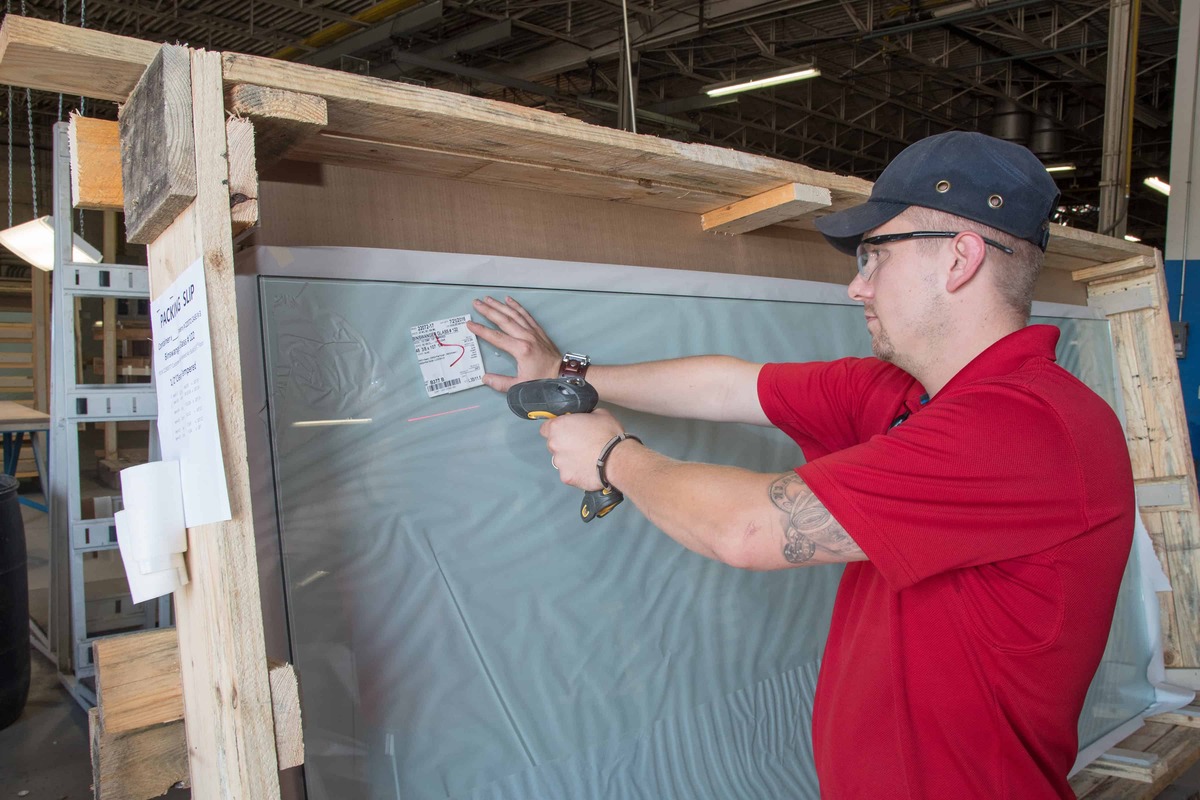 A man operates a power tool to cut through a sheet of glass