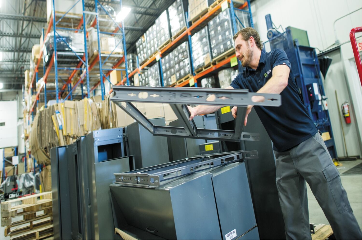 A male worker assembling metal components in a warehouse, surrounded by industrial shelving and equipment, emphasizing efficiency in manufacturing logistics.