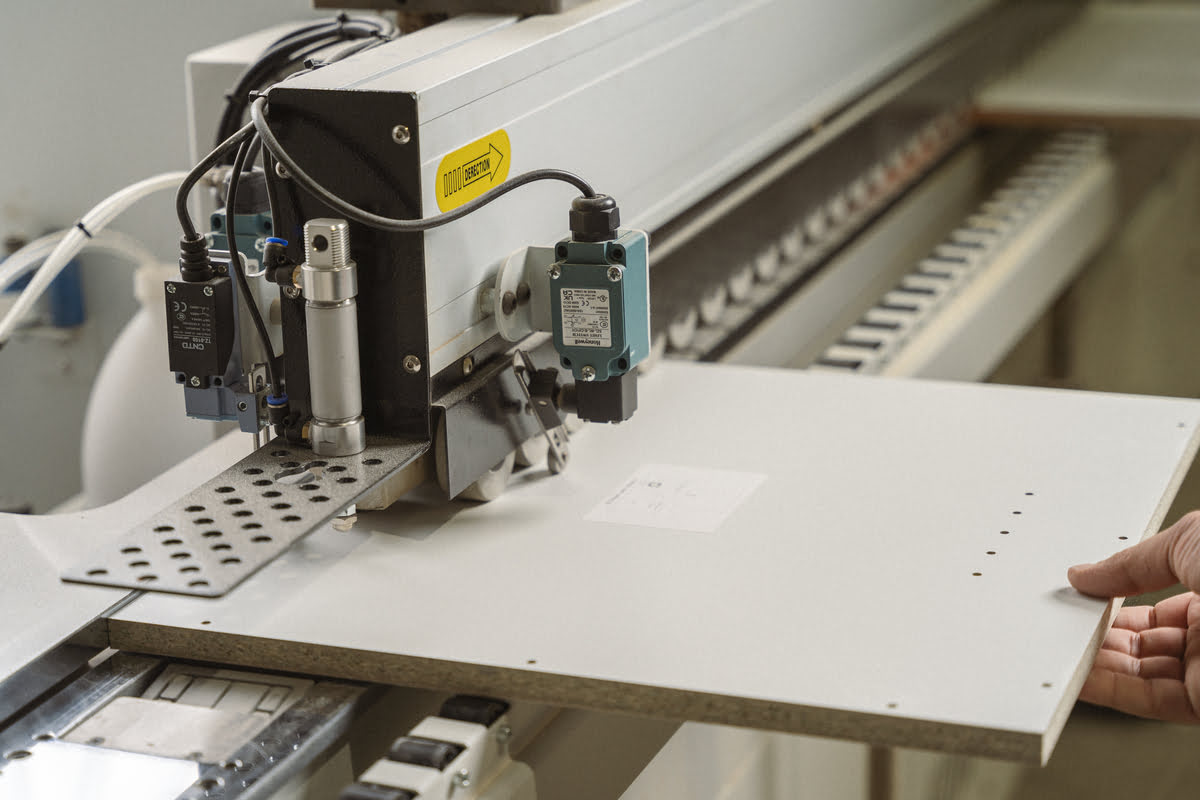 A person operates a machine to cut a piece of wood in a workshop